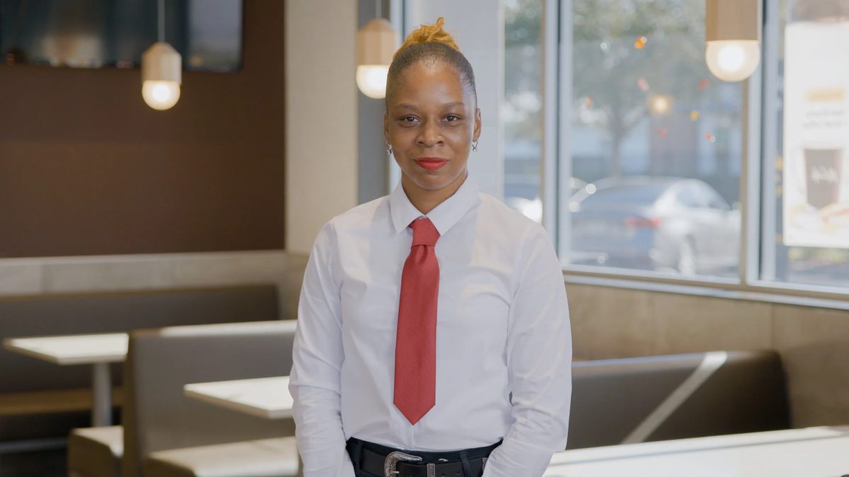 A woman wearing a white shirt and red tie standing inside a McDonald’s restaurant.