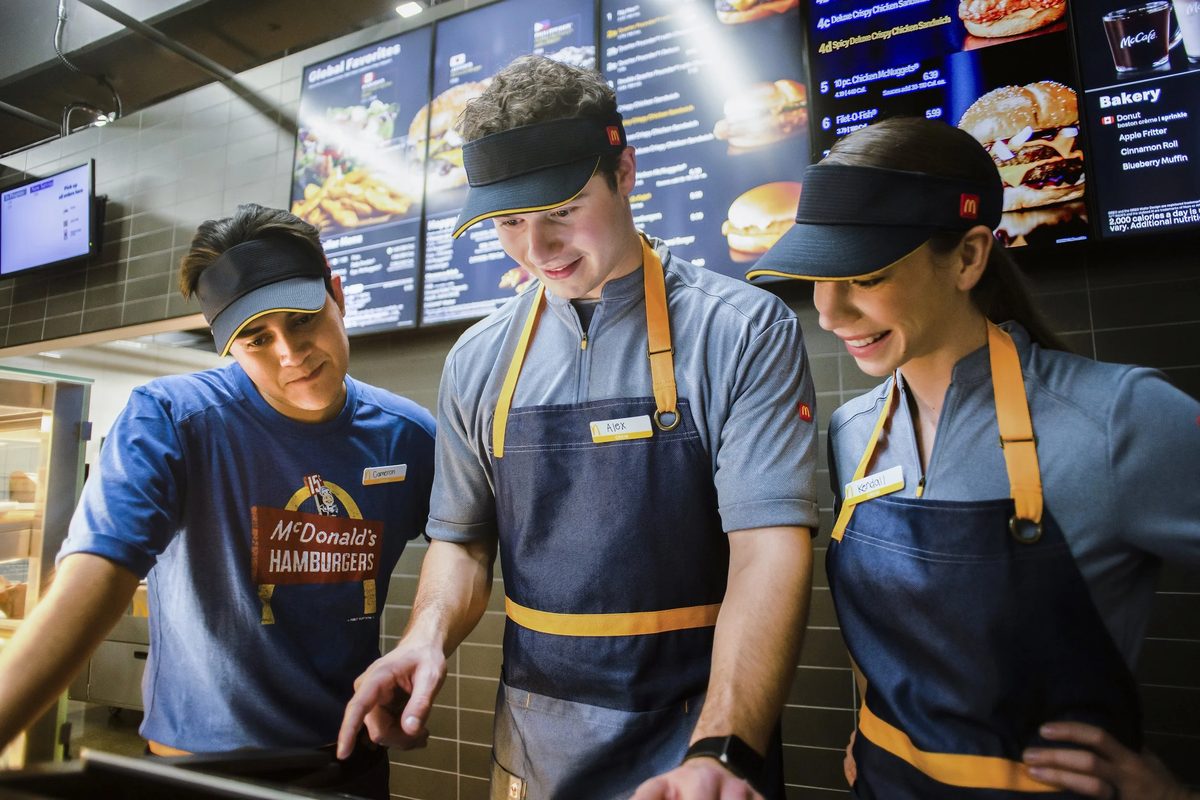 McDonald’s employees working behind the counter, with digital menu boards displaying food options in the background.