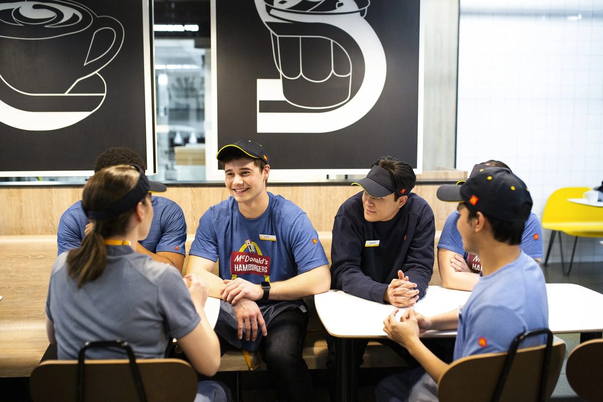 Group of McDonald’s employees in uniform sitting at a table inside the restaurant, engaging in conversation.