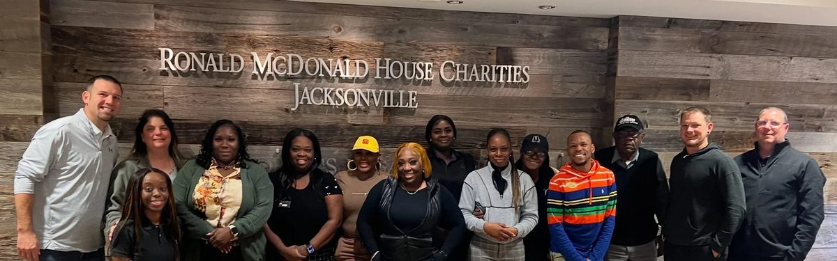A group of people standing in front of a wall with the sign 'Ronald McDonald House Charities Jacksonville'.