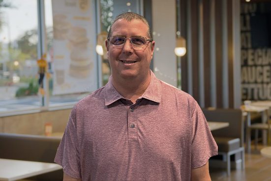 Man in a pink polo shirt and glasses smiling inside a McDonald’s restaurant.